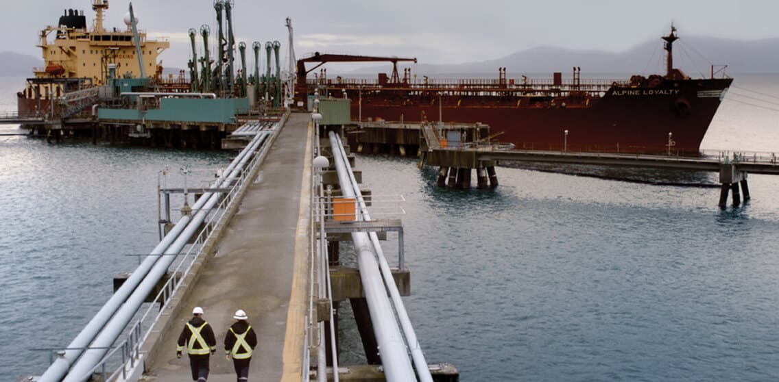 bp case work — two workers walk the pipeline jetty at a marine oil terminal, a tanker berthed alongside